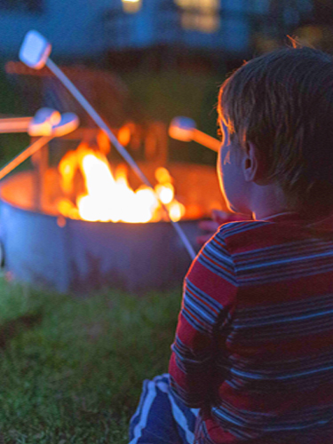 young boy toasting marhsmallows over fire ring