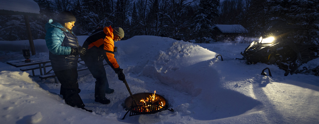 couple at camper cabin in winter with fire ring