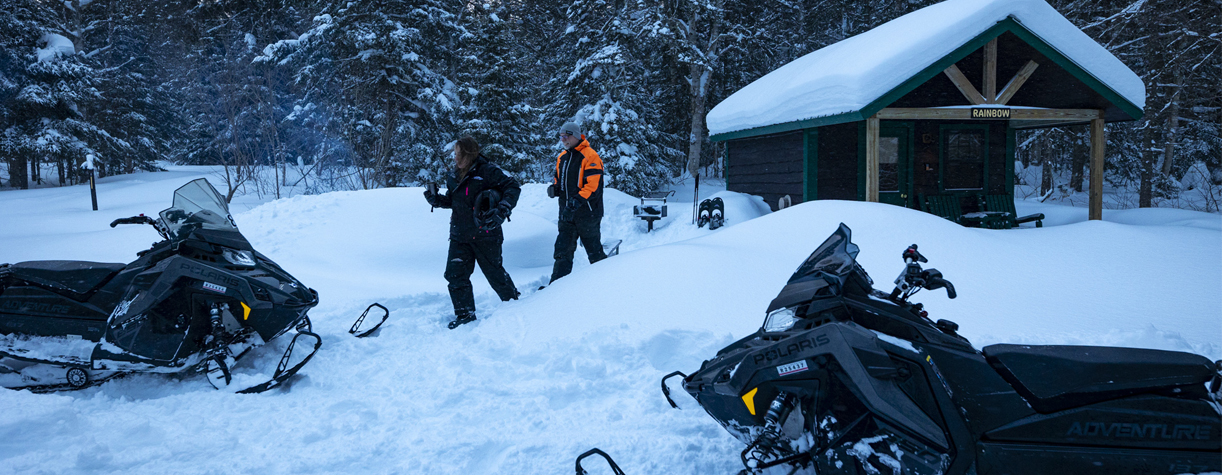 couple outside of a camper cabin snowmobiling